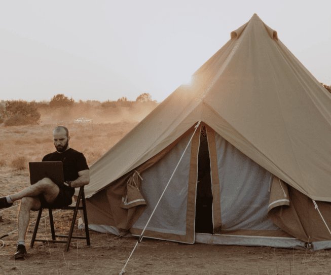 man writing on laptop infront of camping tent